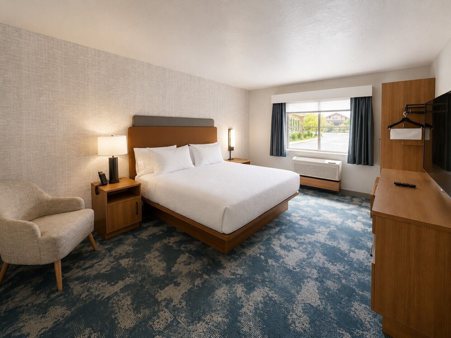 A hotel room with a bed, a chair, a desk, a TV, and a window with curtains.