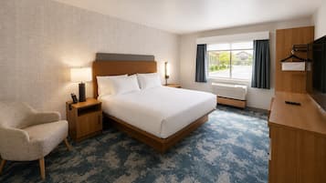 Una habitación de hotel con cama, una silla, escritorio, televisor y ventana con cortinas.