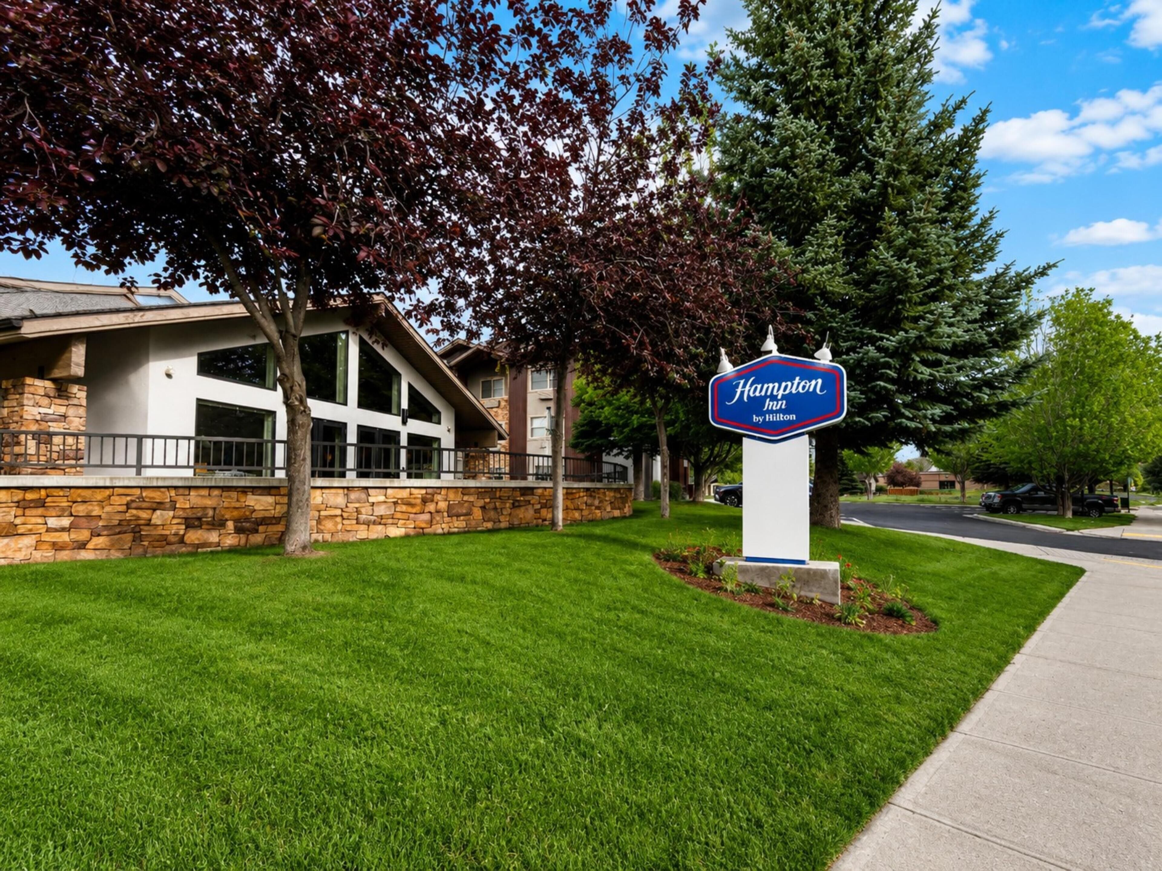 A Hampton Inn by Hilton sign in front of a modern building with stone walls and large windows.