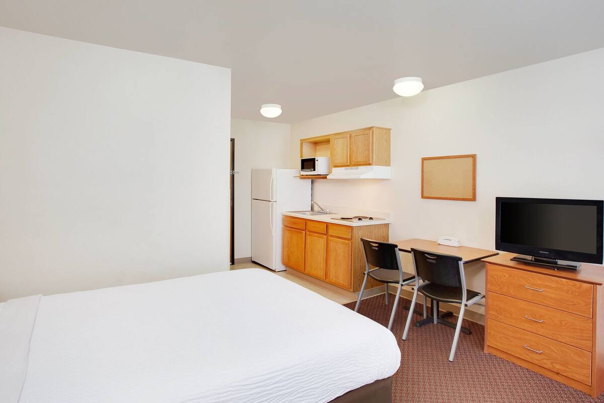 Une chambre d’hôtel de taille réduite, équipée d’un lit, d’un bureau, d’une télévision, d’un four à micro-ondes et d’un réfrigérateur.