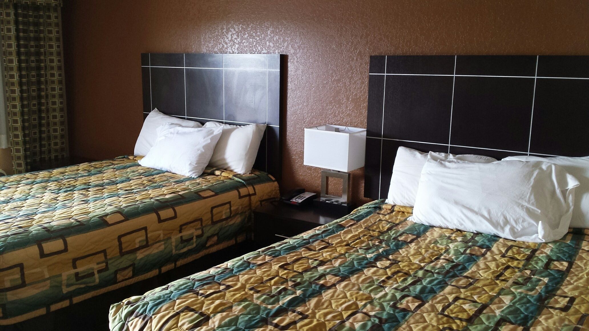 Two twin beds with patterned quilts, a bedside table with a lamp, and a wall-mounted TV.