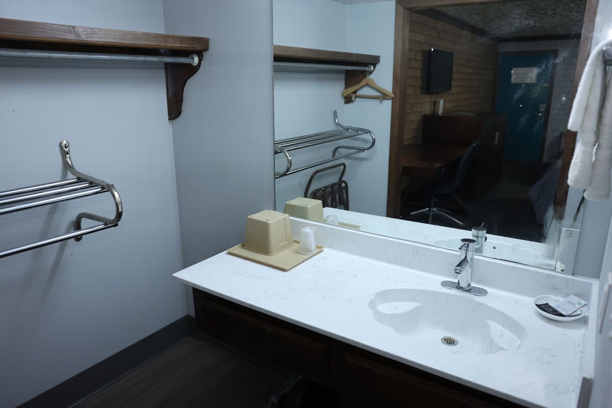 Ein Badezimmer mit einem weißen Waschbecken, Spiegel, Handtuchhalter und einem Holzregal.