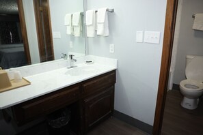 A bathroom with a white sink, dark wooden vanity, a mirror, and a toilet.