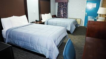 A hotel room with two beds, a desk, a chair, a lamp, and a door with a sign.