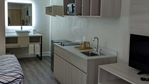 Une chambre d’hôtel de taille réduite, équipée d’une kitchenette, d’un lit, d’une télévision et d’un miroir.