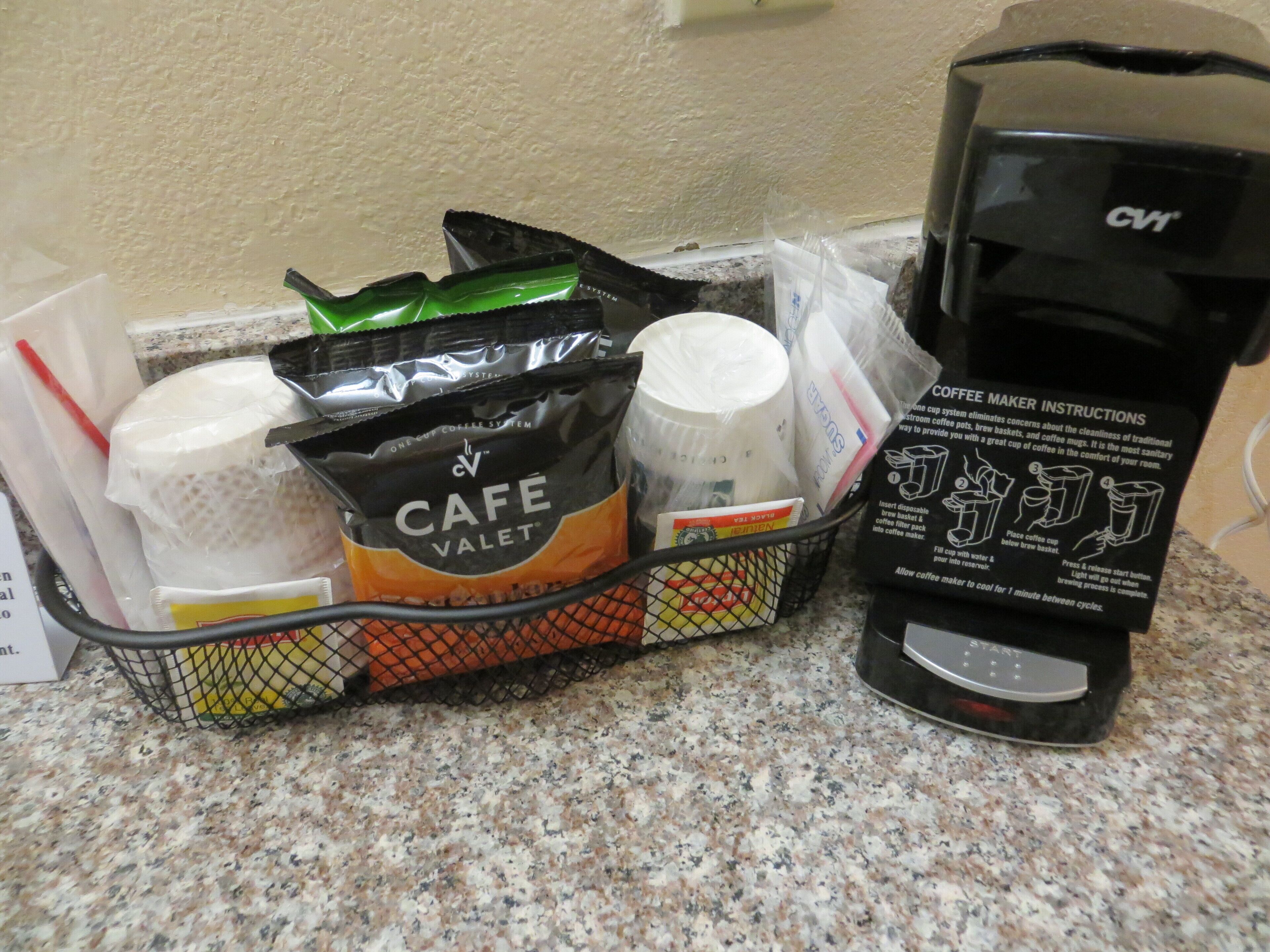 A coffee maker with instructions, a basket containing coffee pods, a plastic cup, and a red straw.