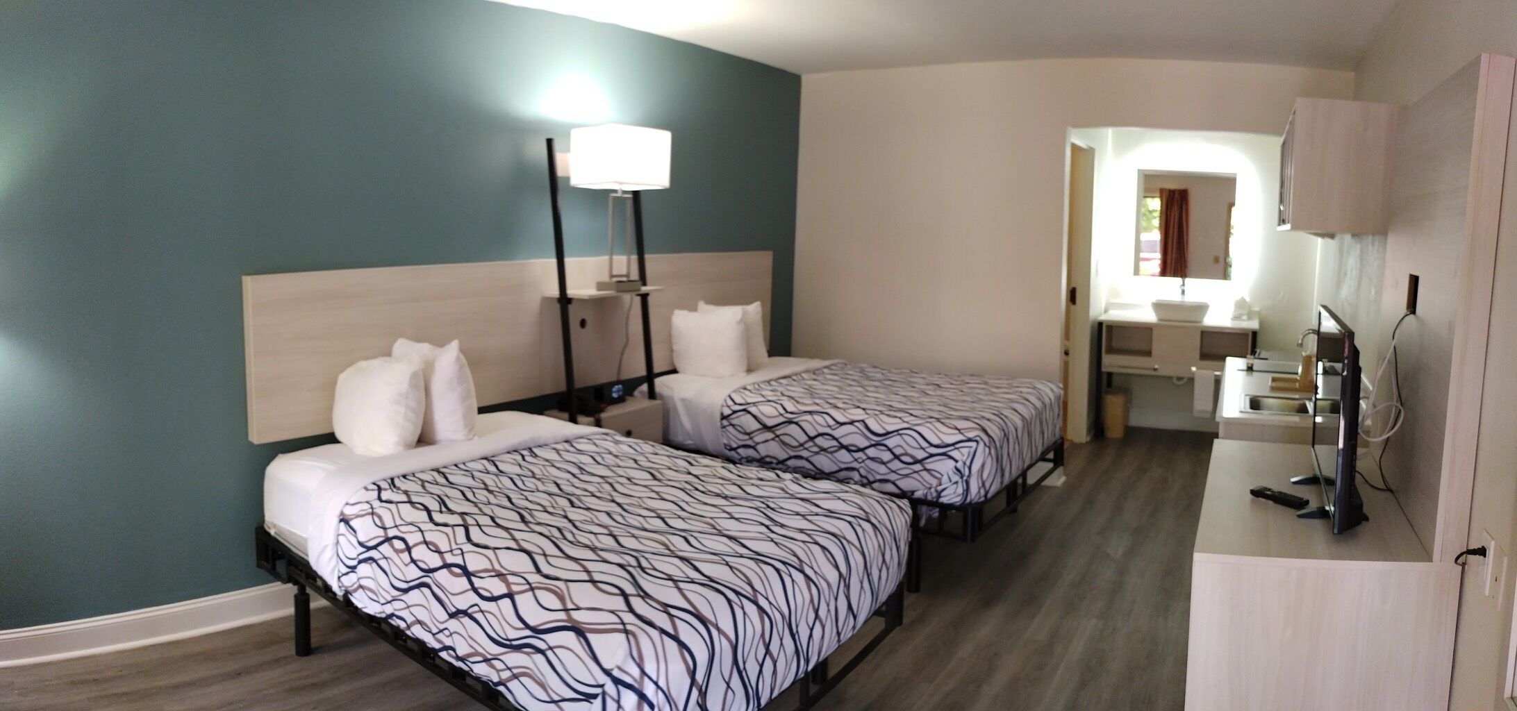 A hotel room with two beds, a desk, a TV, and a bathroom visible through an open doorway.