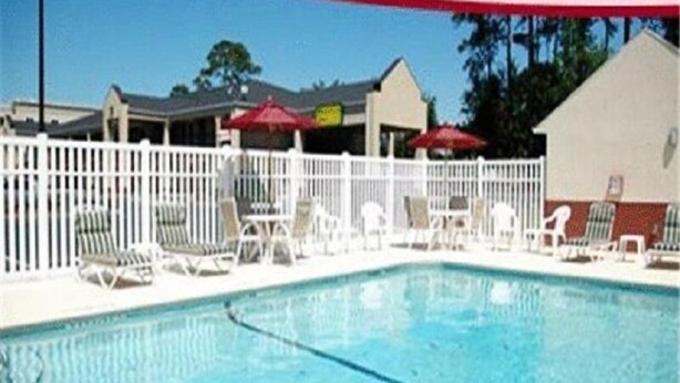 Une piscine entourée d’une clôture blanche, avec des chaises longues et des parasols.