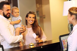 Un mostrador de recepción de hotel con una pantalla digital, un timbre y un huésped sosteniendo una tarjeta.
