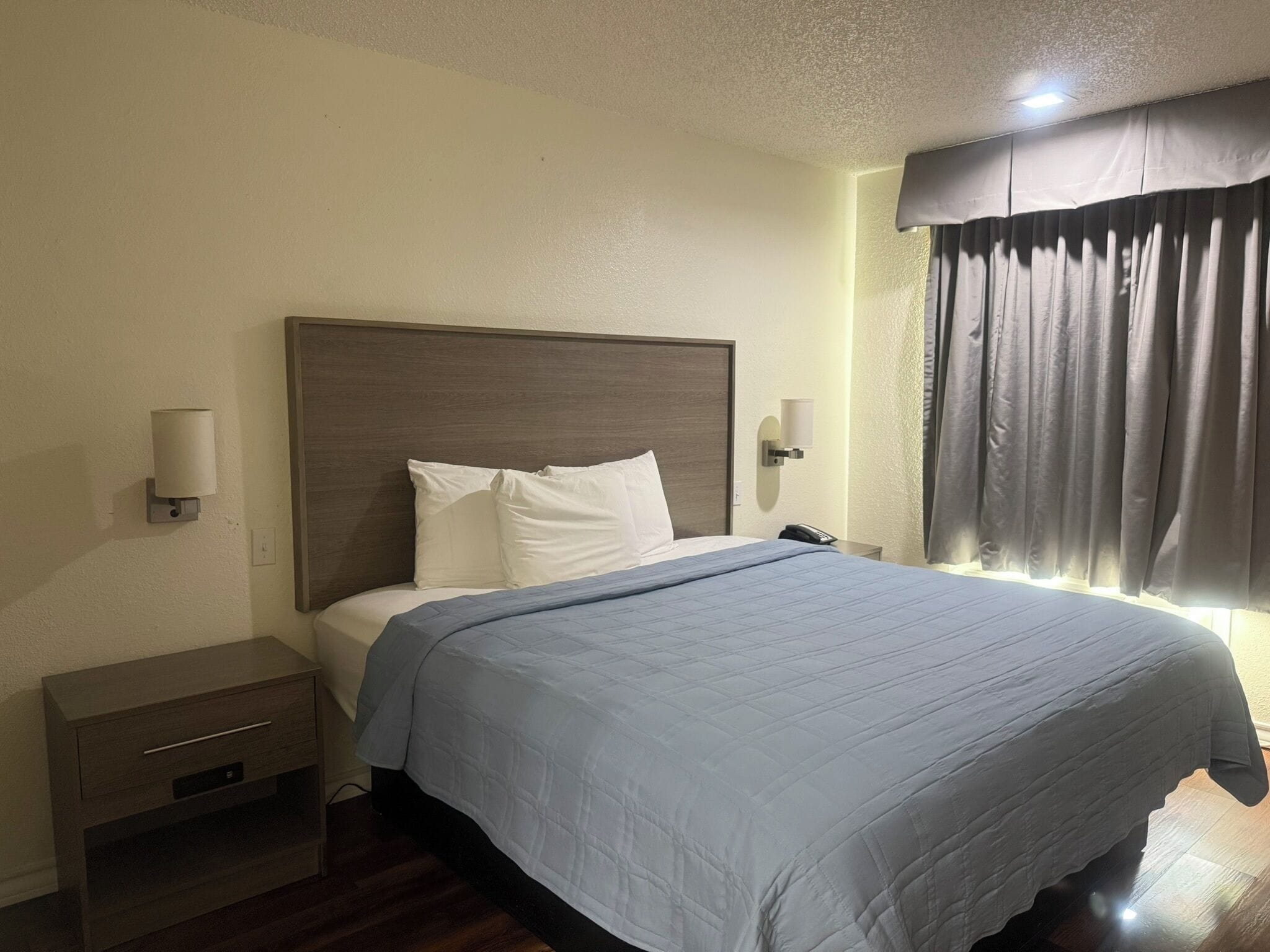 A hotel room with a bed, a nightstand, a lamp, and a window with curtains.