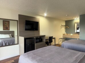 Habitación de hotel con dos camas, un televisor de pantalla plana, un escritorio con silla, un microondas y un tocador con espejo.
