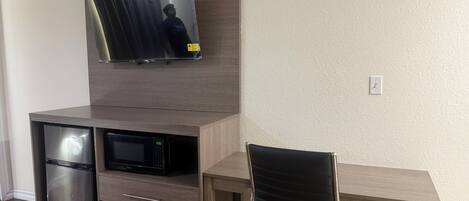 A compact living space with a built-in TV, a small refrigerator, and a desk with a chair.