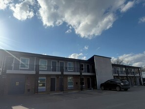 A two-story building with a flat roof, a parking lot, and a black car parked in front.