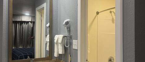 A bathroom with a granite countertop sink, a mirror, a hairdryer, and a shower area.