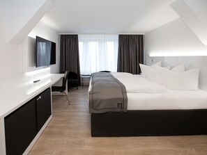 Una habitación de hotel moderna con cama, escritorio, silla, televisor y ventana con cortinas.