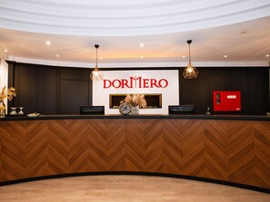 Zona de recepción de un hotel con diseño moderno, que presenta un amplio mostrador, una chimenea y una caja roja de equipo de emergencia.