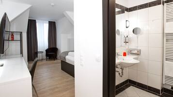 Quarto de hotel moderno com uma cama grande, uma escrivaninha com cadeira, uma mesinha e um espelho.