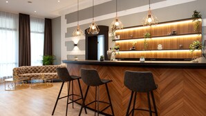 Un espace bar moderne avec un revêtement de sol en bois disposé en chevrons, trois tabourets de bar et des luminaires suspendus.
