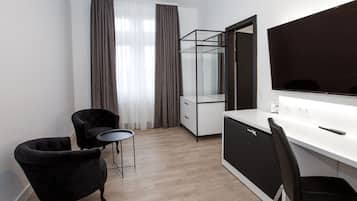 Quarto moderno e minimalista com escrivaninha branca, duas cadeiras pretas, um espelho grande e uma televisão.