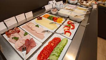 Un bufé con diversas opciones de comida, incluyendo carnes, quesos y verduras.