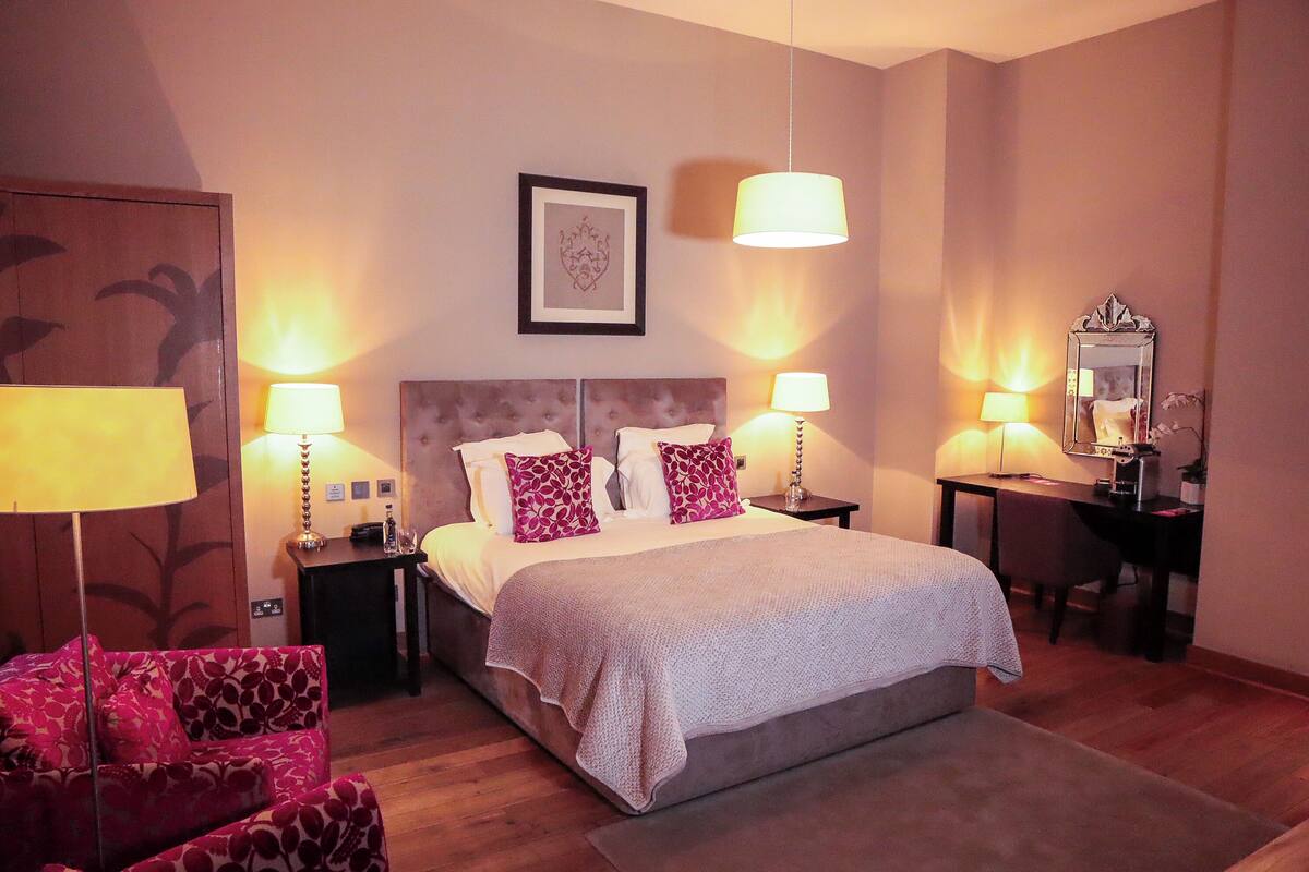 Habitación de hotel con una cama grande, dos mesitas de noche con lámparas, un escritorio con espejo y una silla.