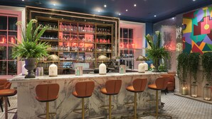 A bar area with marble counters, gold chairs, and a variety of bottles and glasses on shelves. - Tigerlily (Edinburgh)