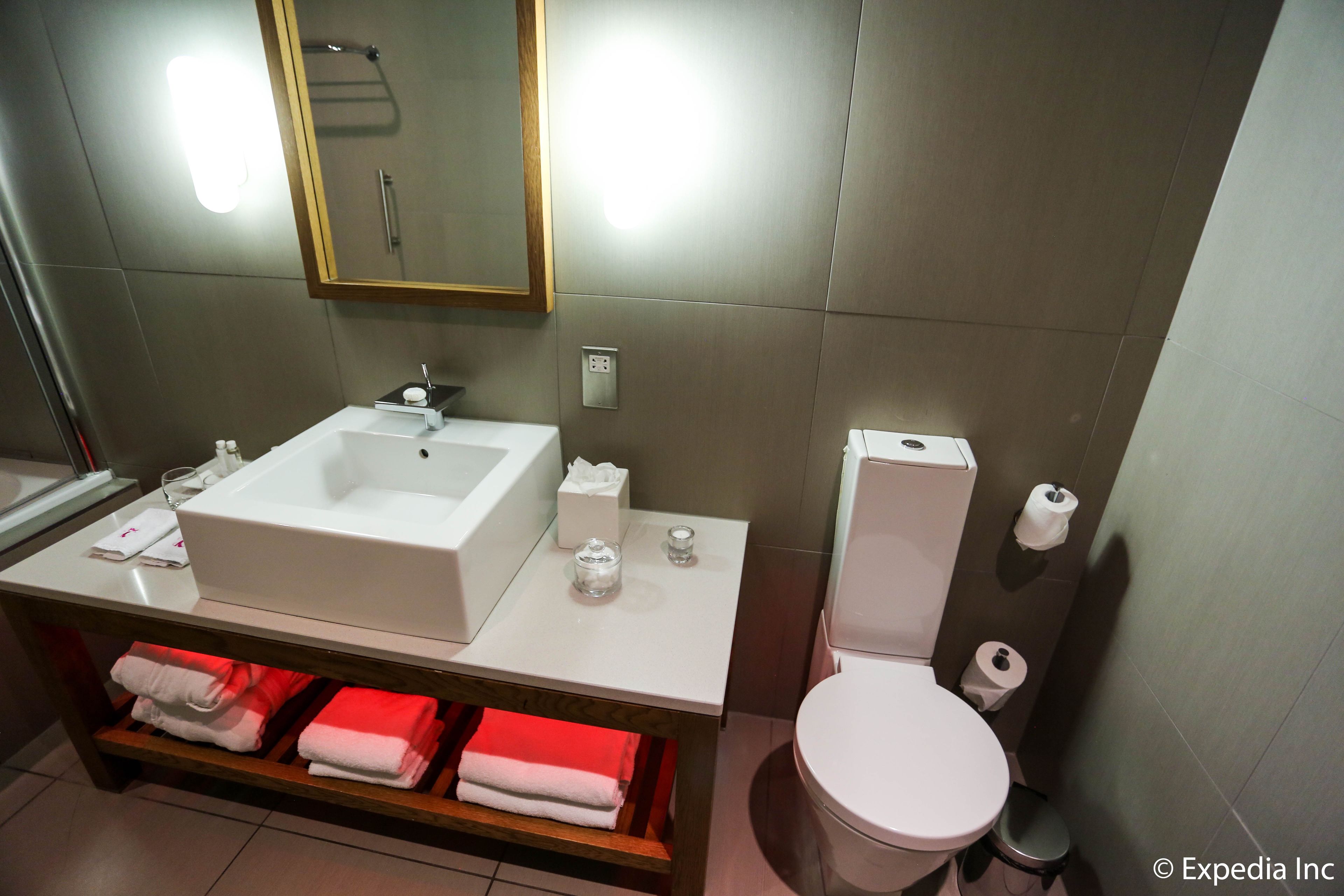 A modern bathroom with a white sink, mirror, and toilet. There are towels and toiletries on the counter.