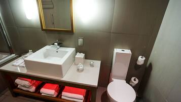 A modern bathroom with a white sink, mirror, and toilet. There are towels and toiletries on the counter.