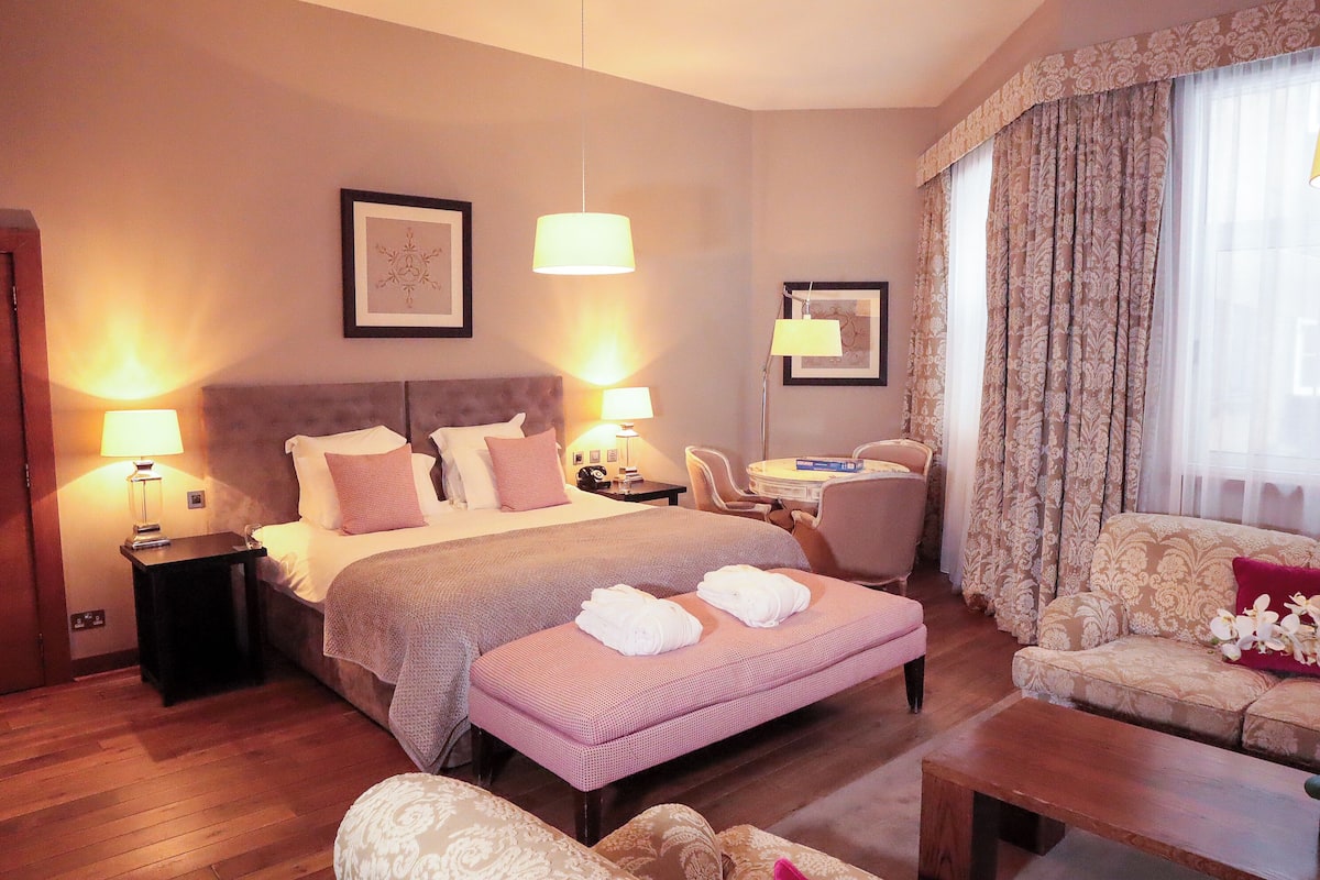 Una habitación de hotel con una cama grande, mesitas de noche con lámparas, un sofá, una pequeña mesa y una silla.