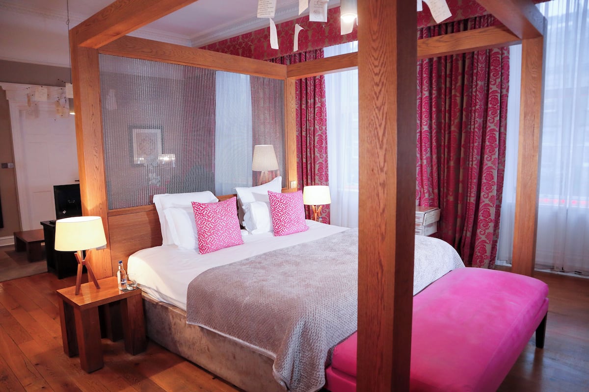 Una cama con dosel sobre cuatro soportes, con estructura de madera, un espejo grande y una decoración en tonos rosa y blanco.