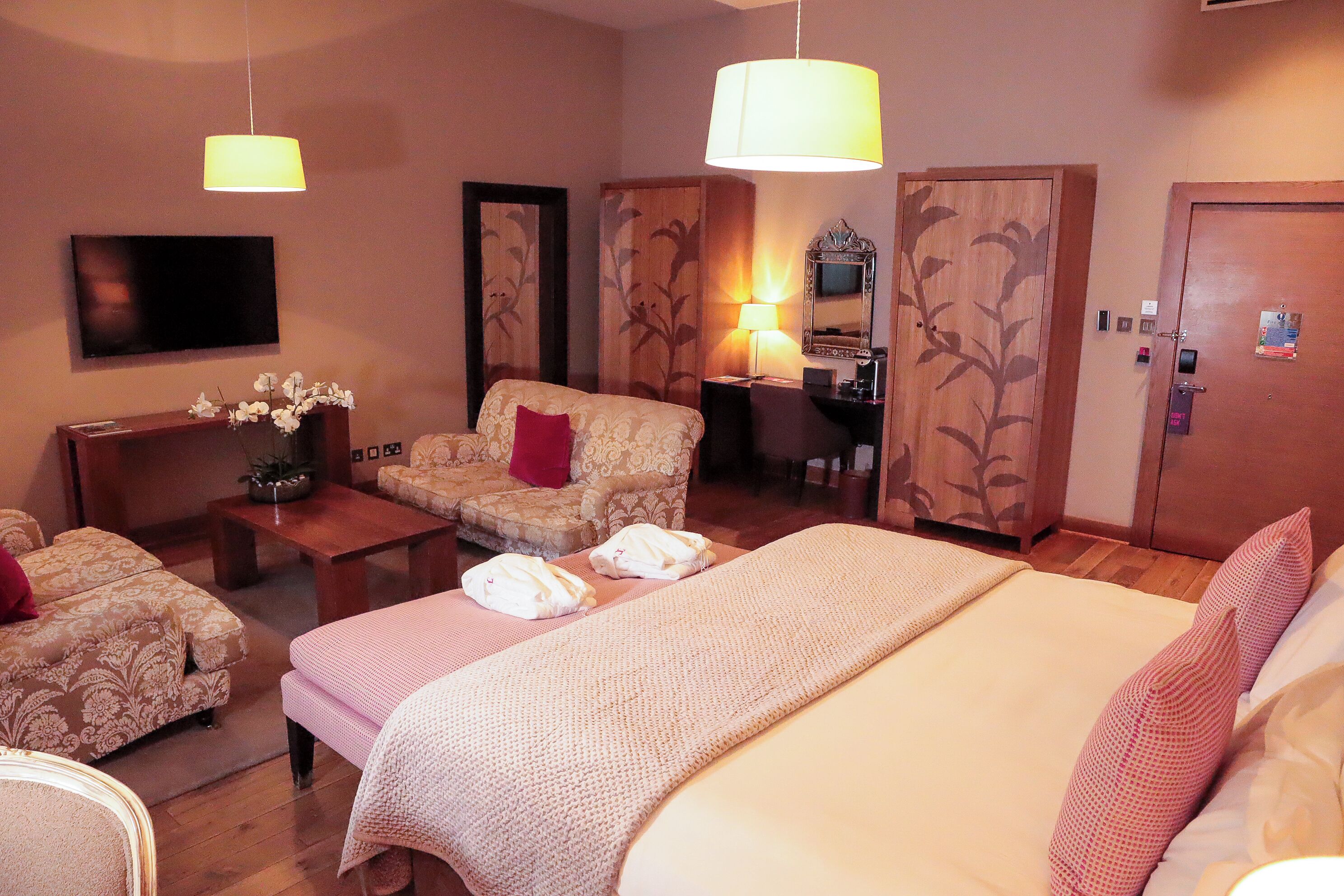 Quarto de hotel com uma cama grande, um sofá, uma escrivaninha e uma televisão.