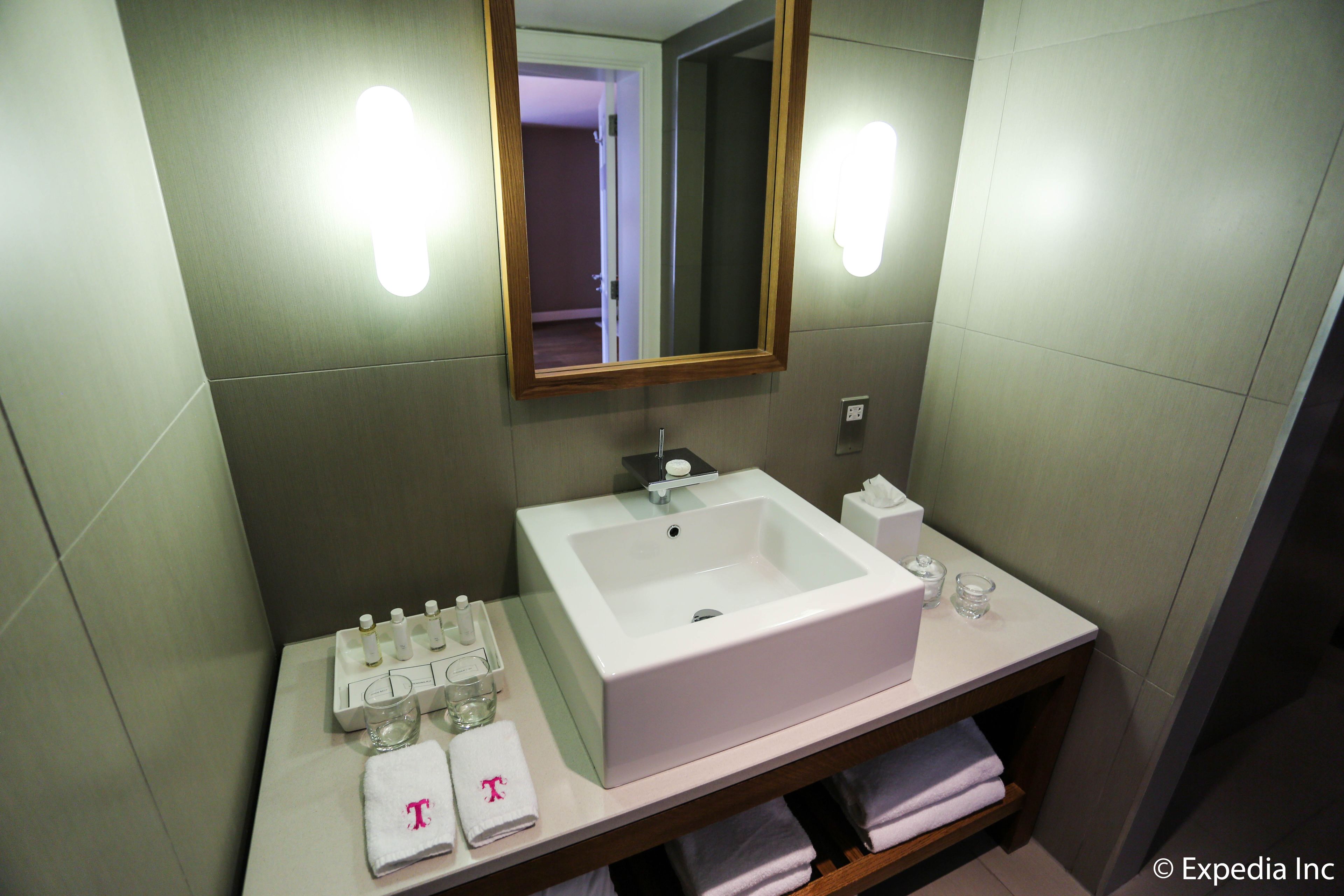 A bathroom with a white sink, mirror, and towel rack. There are toiletries on the counter and a glass of water.