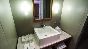 A bathroom with a white sink, mirror, and towel rack. There are toiletries on the counter and a glass of water.