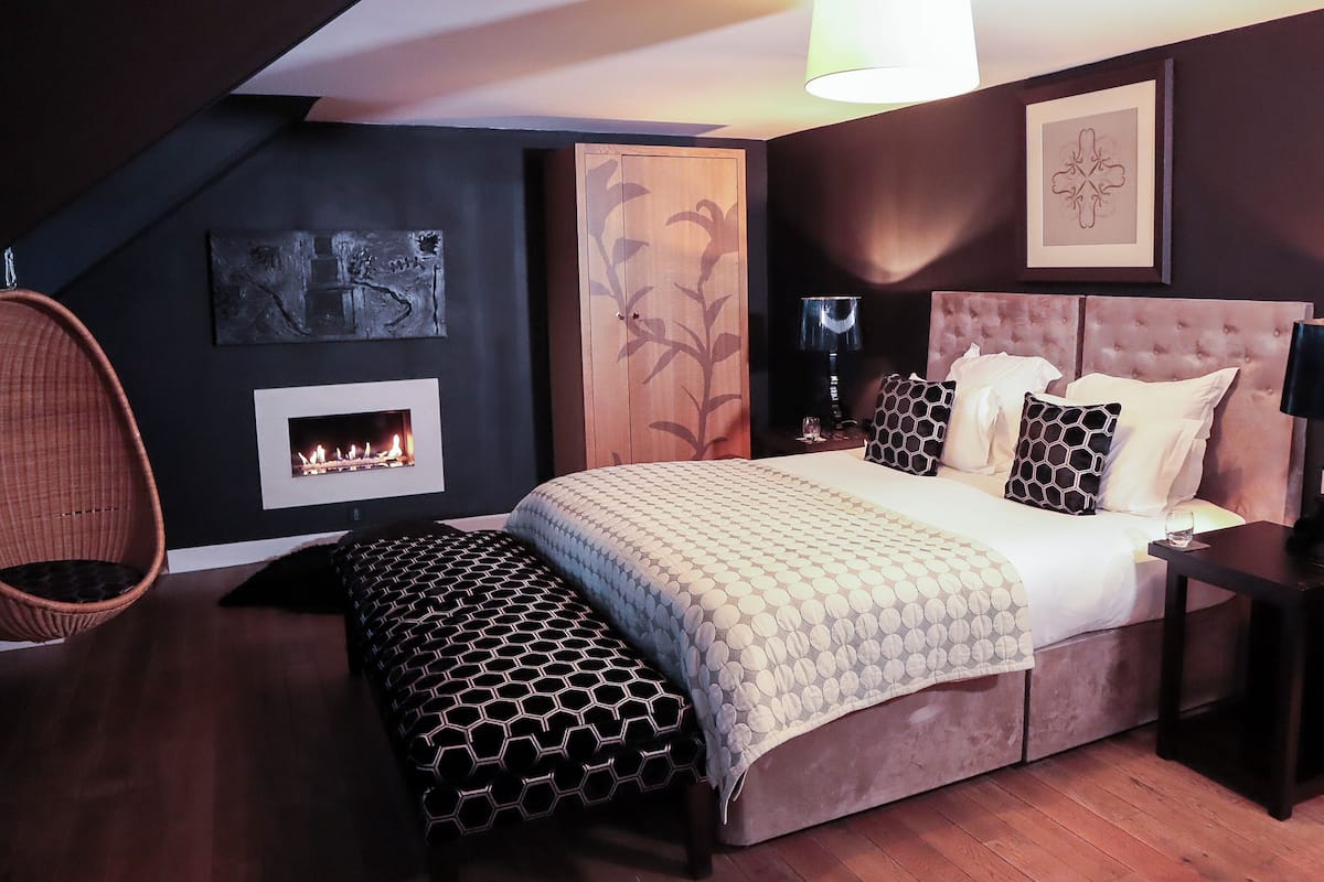 Un dormitorio con una cama grande, una chimenea, una silla colgante y obras de arte en las paredes.