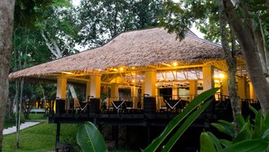 A thatched-roof structure with outdoor seating, surrounded by trees.