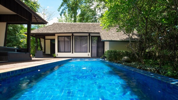 A swimming pool with a tiled edge, surrounded by a wooden deck and a covered seating area.