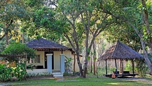 A small, single-story building with a tiled roof, surrounded by lush greenery and trees.
