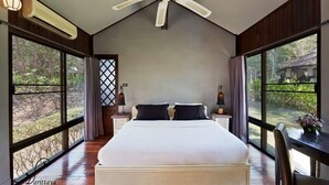 A spacious bedroom with a large bed, a ceiling fan, and large windows offering a view of the outdoors.