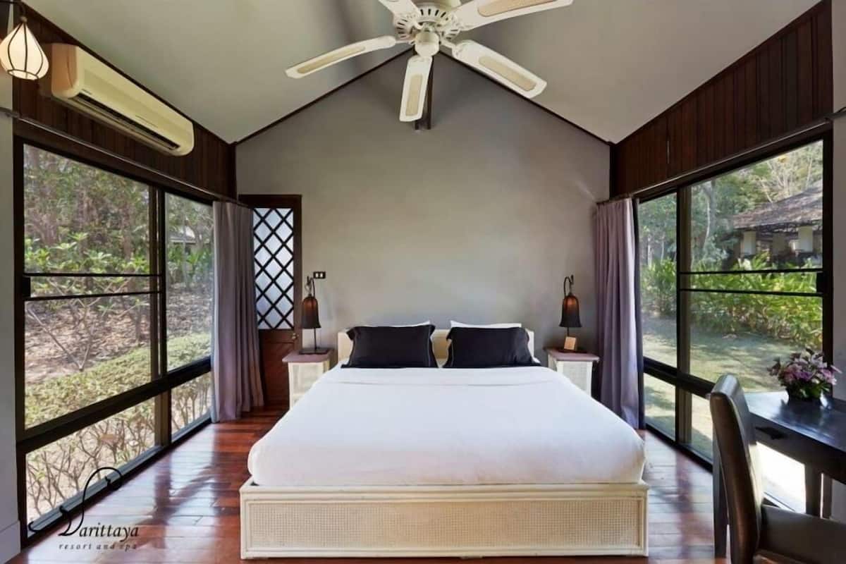A spacious bedroom with a large bed, a ceiling fan, and large windows offering a view of the outdoors.