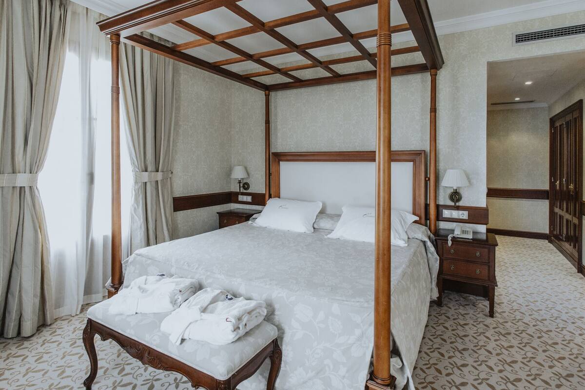 A four-poster bed with a wooden frame, a bedside table with a lamp, and a bathroom with a toilet and a mirror.