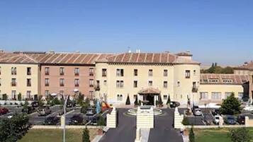 A large building with a central courtyard, multiple floors, and a parking area in front.