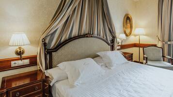 A hotel room with a four-poster bed, a nightstand with a lamp, a chair, and a mirror on the wall.