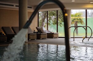 A pool area with lounge chairs and a person sitting by the window.