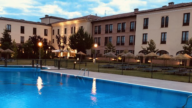 A swimming pool surrounded by lounge chairs and umbrellas, with buildings in the background.