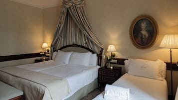 A hotel room with two beds, a canopy bed, a nightstand with a lamp, a framed portrait, and a vase with flowers.