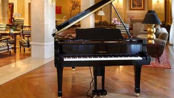 Un piano de cola Yamaha negro en un vestíbulo luminoso con suelo de mármol, un sofá y una lámpara.