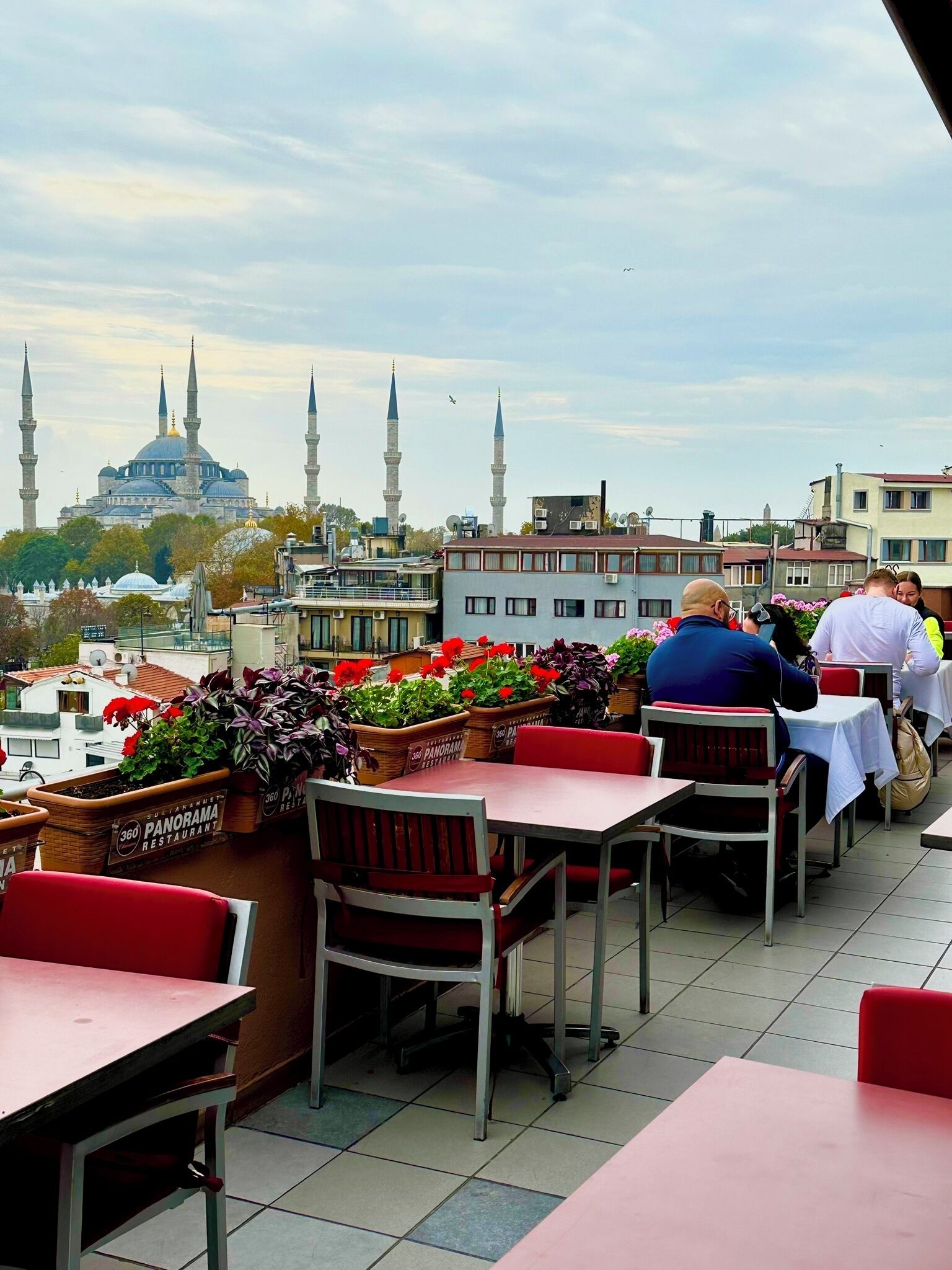 A restaurant with outdoor seating overlooking a cityscape, featuring a view of a mosque with multiple minarets.