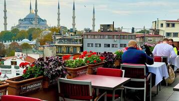 A restaurant with outdoor seating overlooking a cityscape, featuring a view of a mosque with multiple minarets.