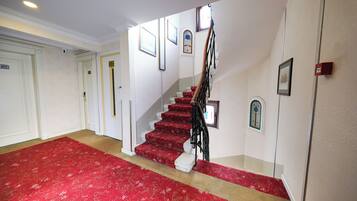 A staircase with red carpet leading to a landing, white walls, and framed pictures.