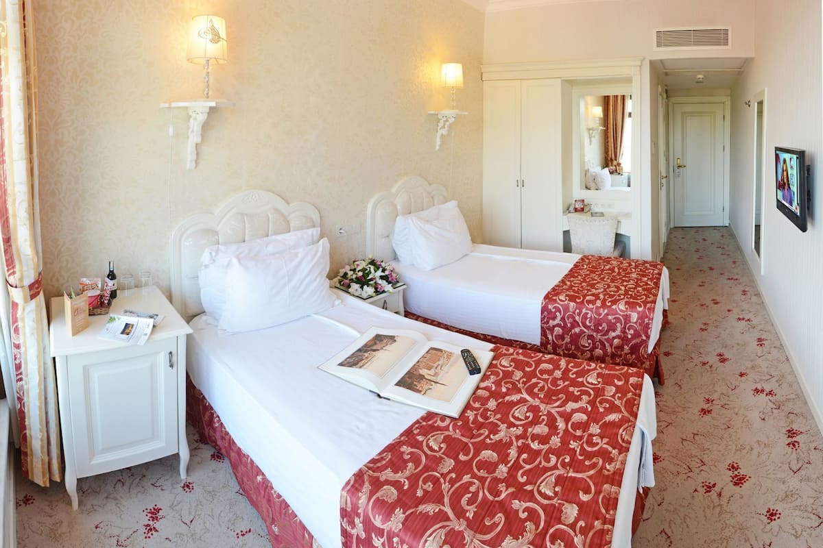 A hotel room with two beds, a nightstand, a mirror, and a television.